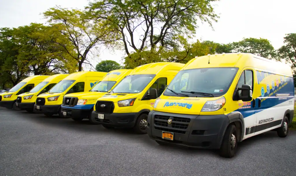 A row of yellow and blue delivery vans is parked on an asphalt lot with trees in the background, ready to serve as your trusted Lennox Premier Dealer with flexible finance options.