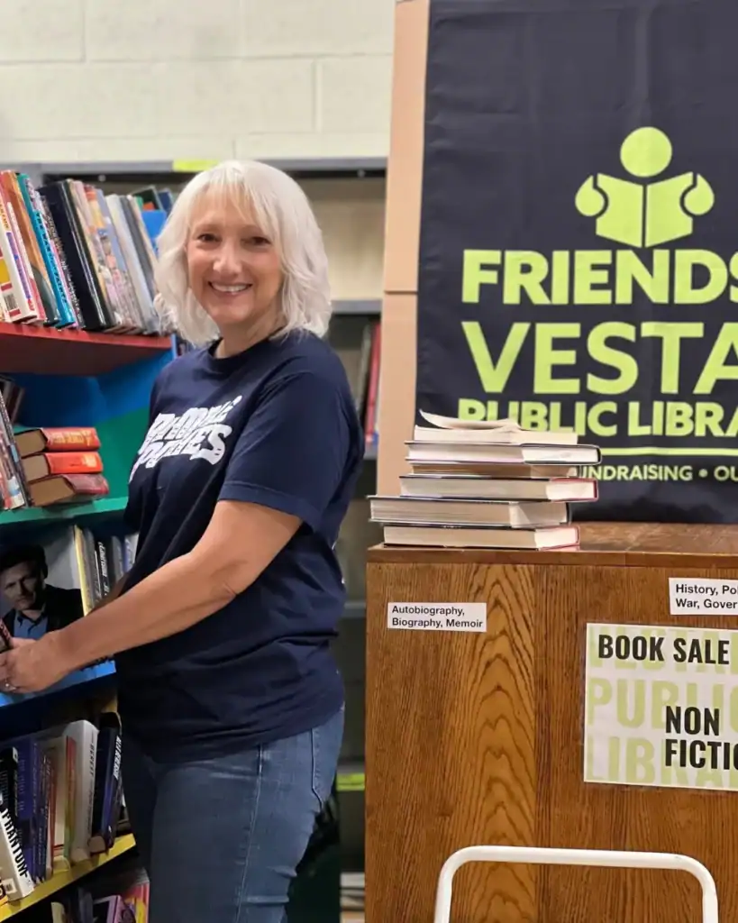 A smiling woman organizes books at an Auchinachie Cares library book sale.
